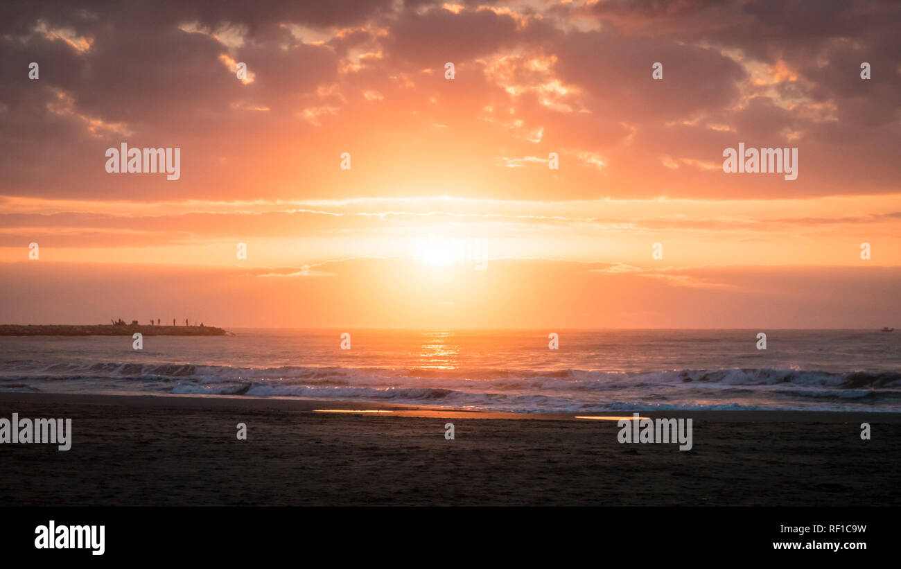 Una bella foto di sole luminoso tra il Mar Mediterraneo e il drammatico cielo nuvoloso al sunrise in Cullera, regione di Valencia, Spagna. Foto Stock
