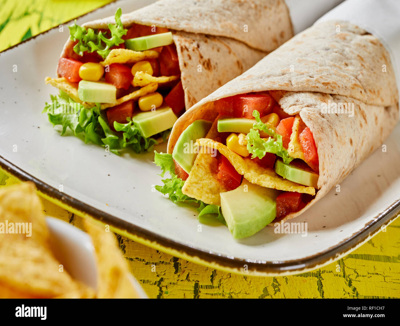 Deliziosa tortilla avvolge con fresche avocado, insalata ingredienti e nachos su una piastra rettangolare per uno spuntino in una vista ravvicinata Foto Stock