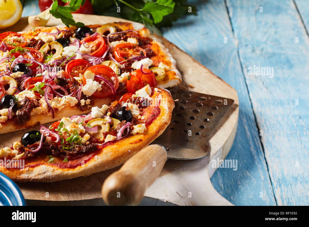 Tradizionale greco per la pizza con il formaggio feta e olive farcite con il coriandolo fresco servito su un vecchio tagliere di legno in una vista ravvicinata con copia Foto Stock