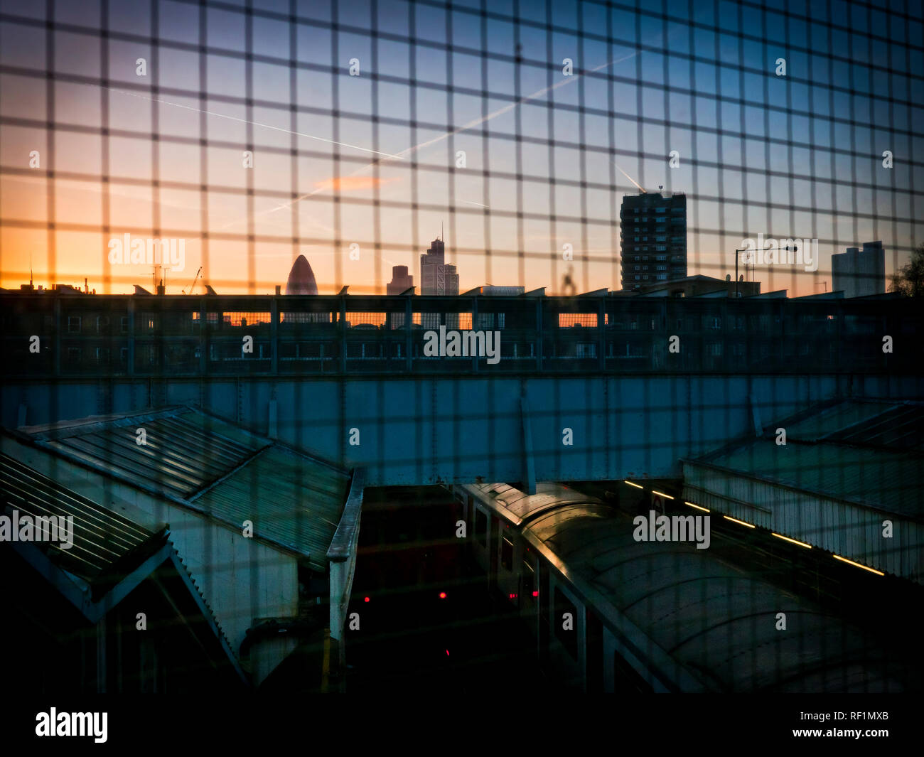Una vista dal vecchio ponte pedonale che collegava entrambi District Line piattaforme a Whitechapel Station di Londra verso lo skyline della città al crepuscolo Foto Stock