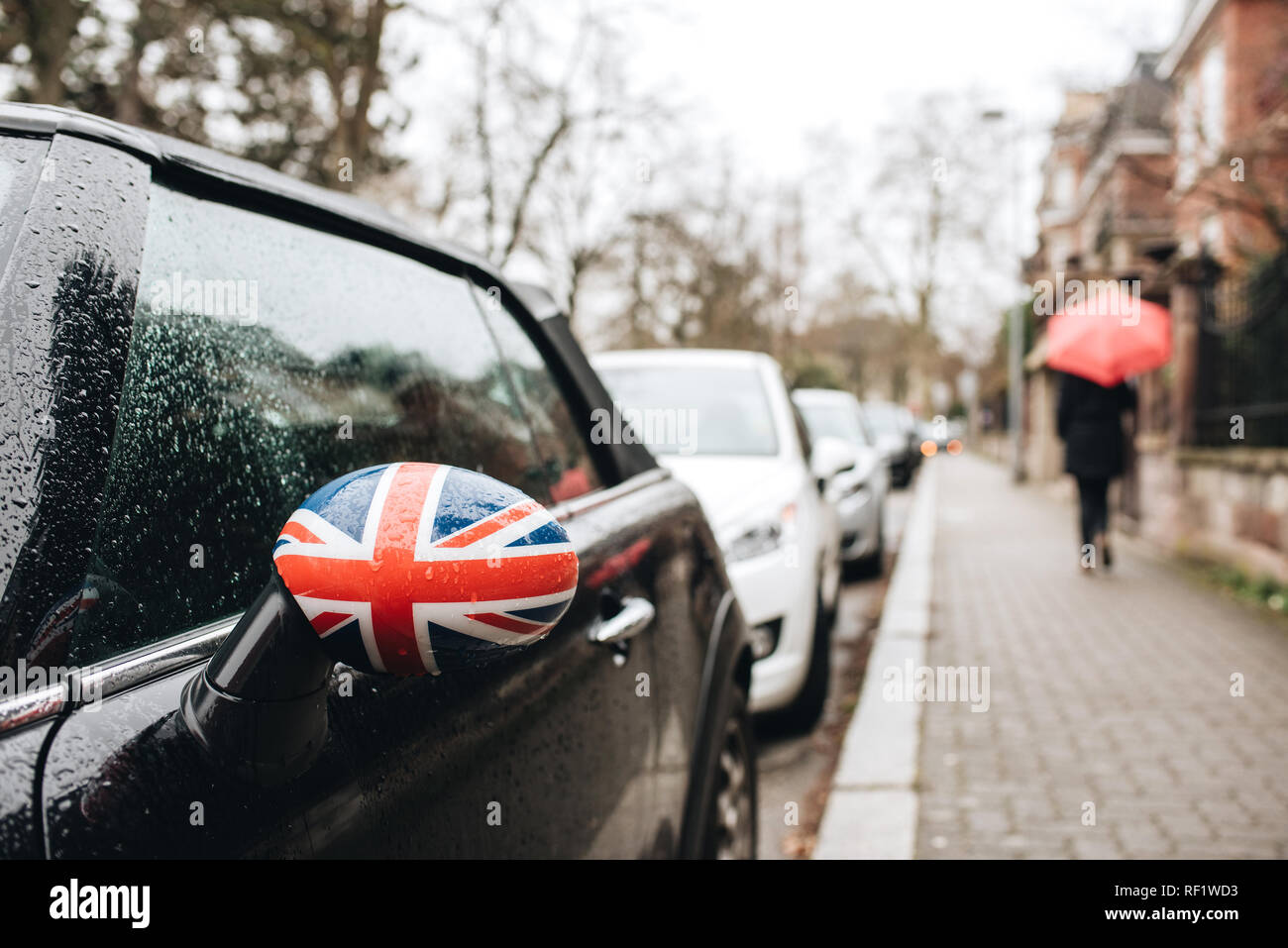 Bandiera britannica Union Jack su uno specchio auto con silhouette di donna con ombrello in un giorno di pioggia nella città francese a piedi Foto Stock