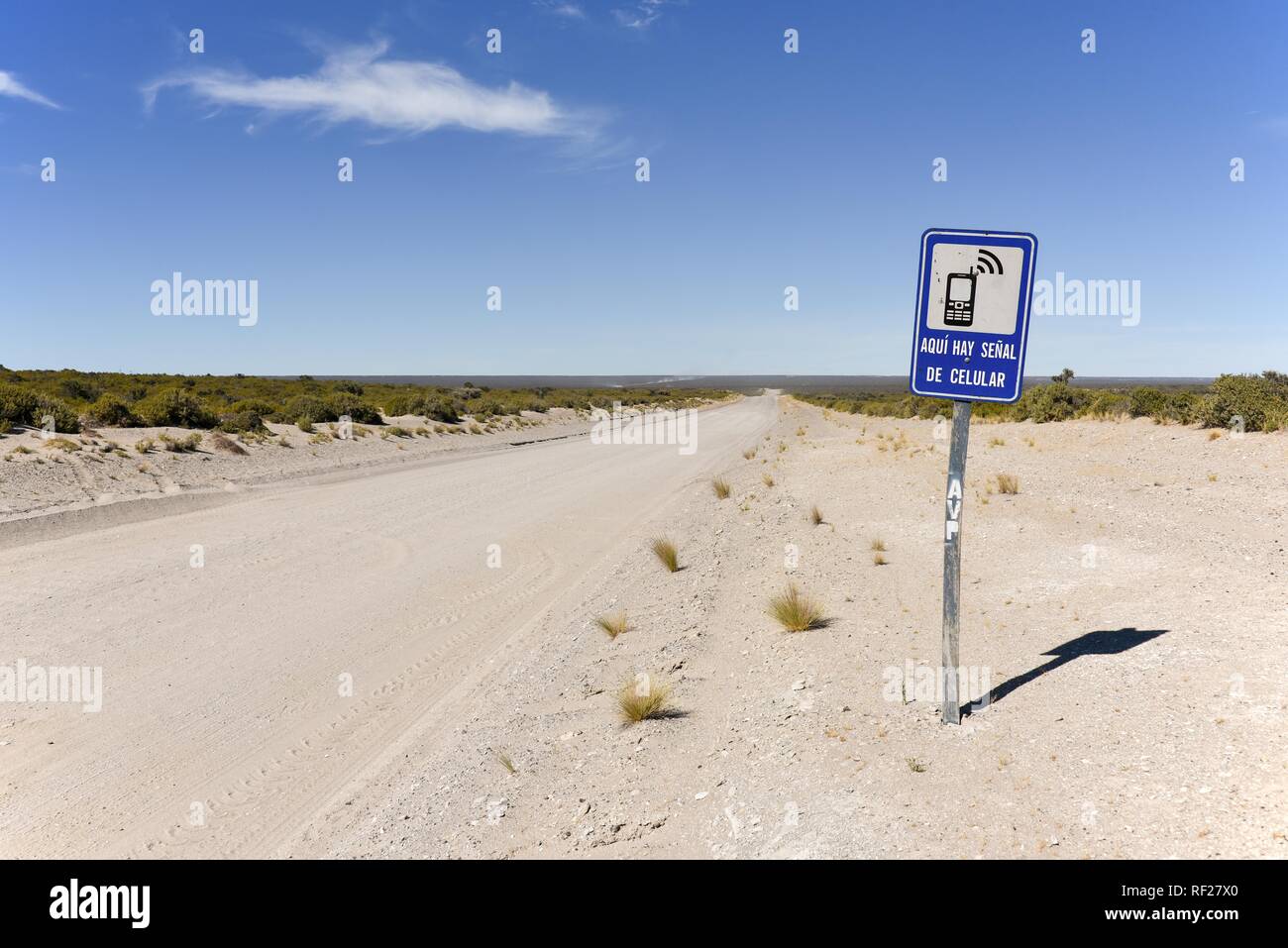 Cartello per un posto con telefono mobile reception accanto a infinite strada di ghiaia, deserto della Penisola Valdes, Patagonia Foto Stock