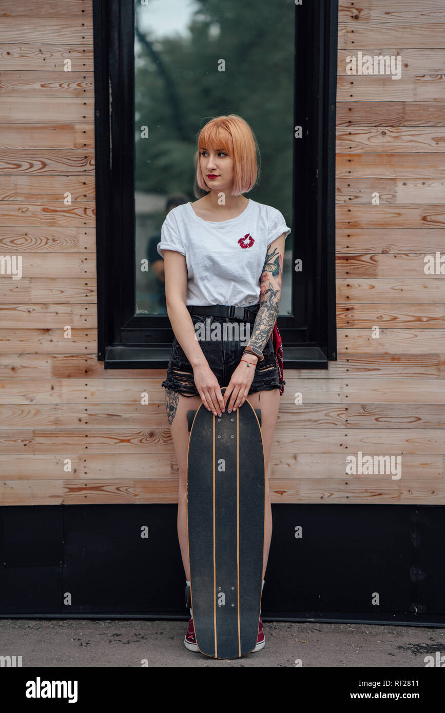 Giovane donna in piedi fuori dall'edificio con carver skateboard Foto Stock