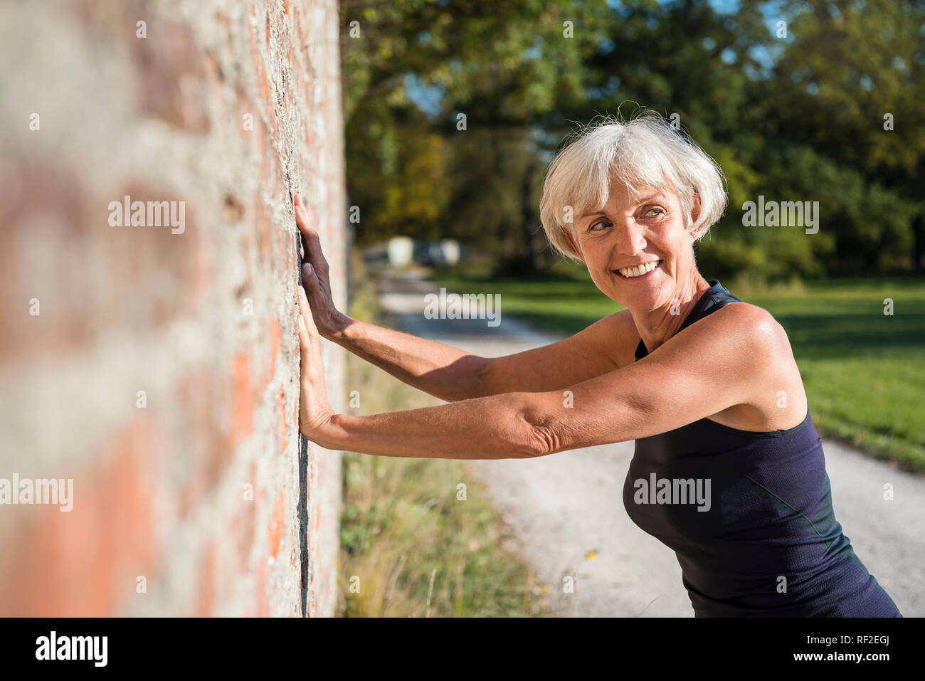 Sorridente senior sportive donna appoggiata contro un muro di mattoni Foto Stock