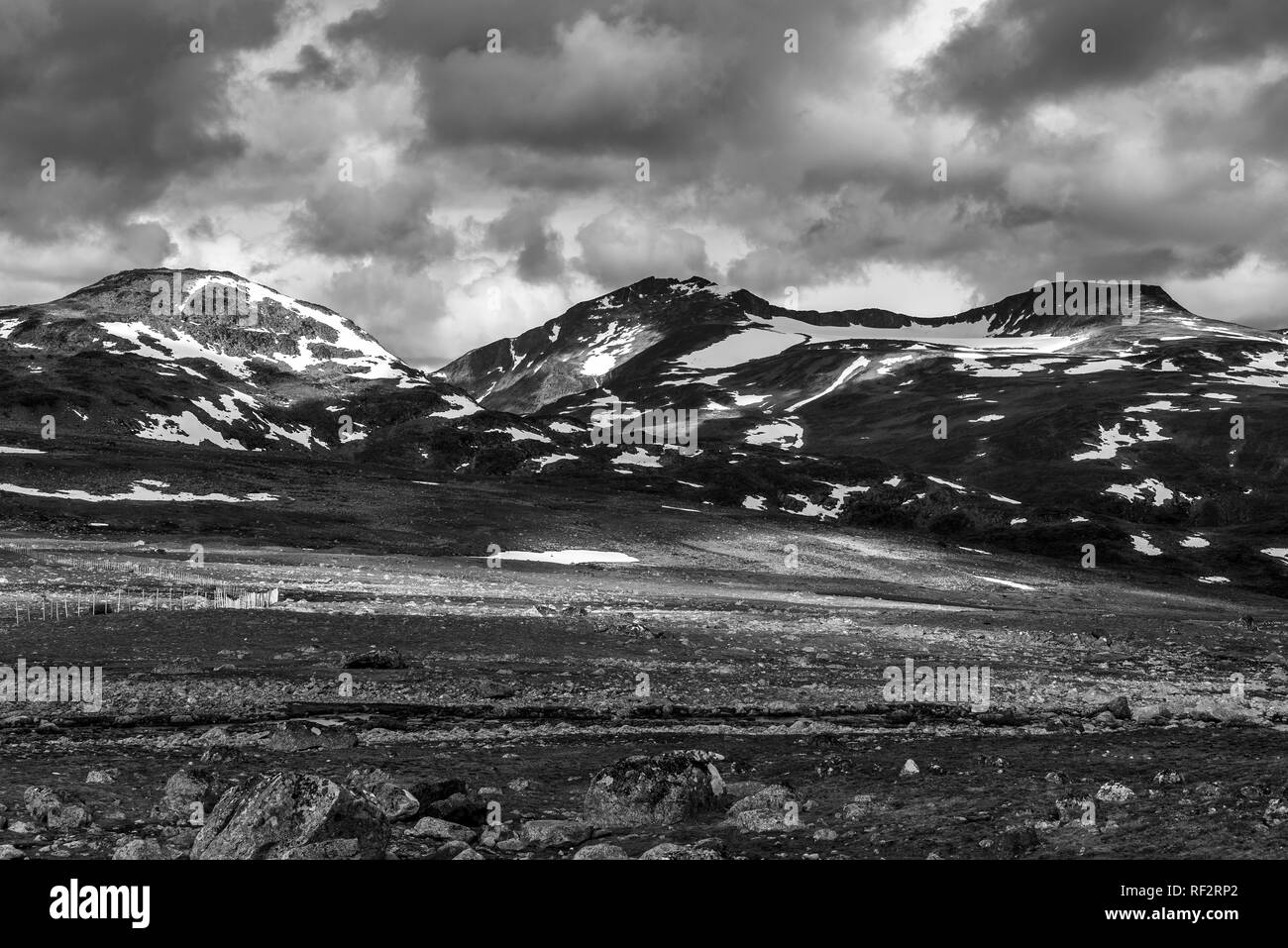 Una vista di rocky e terreno in pietra con nuvole temporalesche coperti con le montagne sullo sfondo. Norvegia, intorno a Beitostolen. Foto Stock