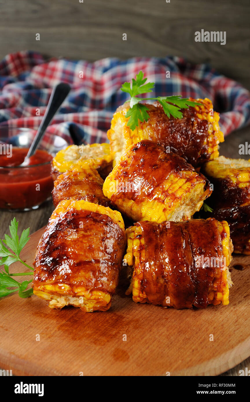 Mais alla brace avvolto con fette di pancetta sotto BBQ SAUCE Foto Stock