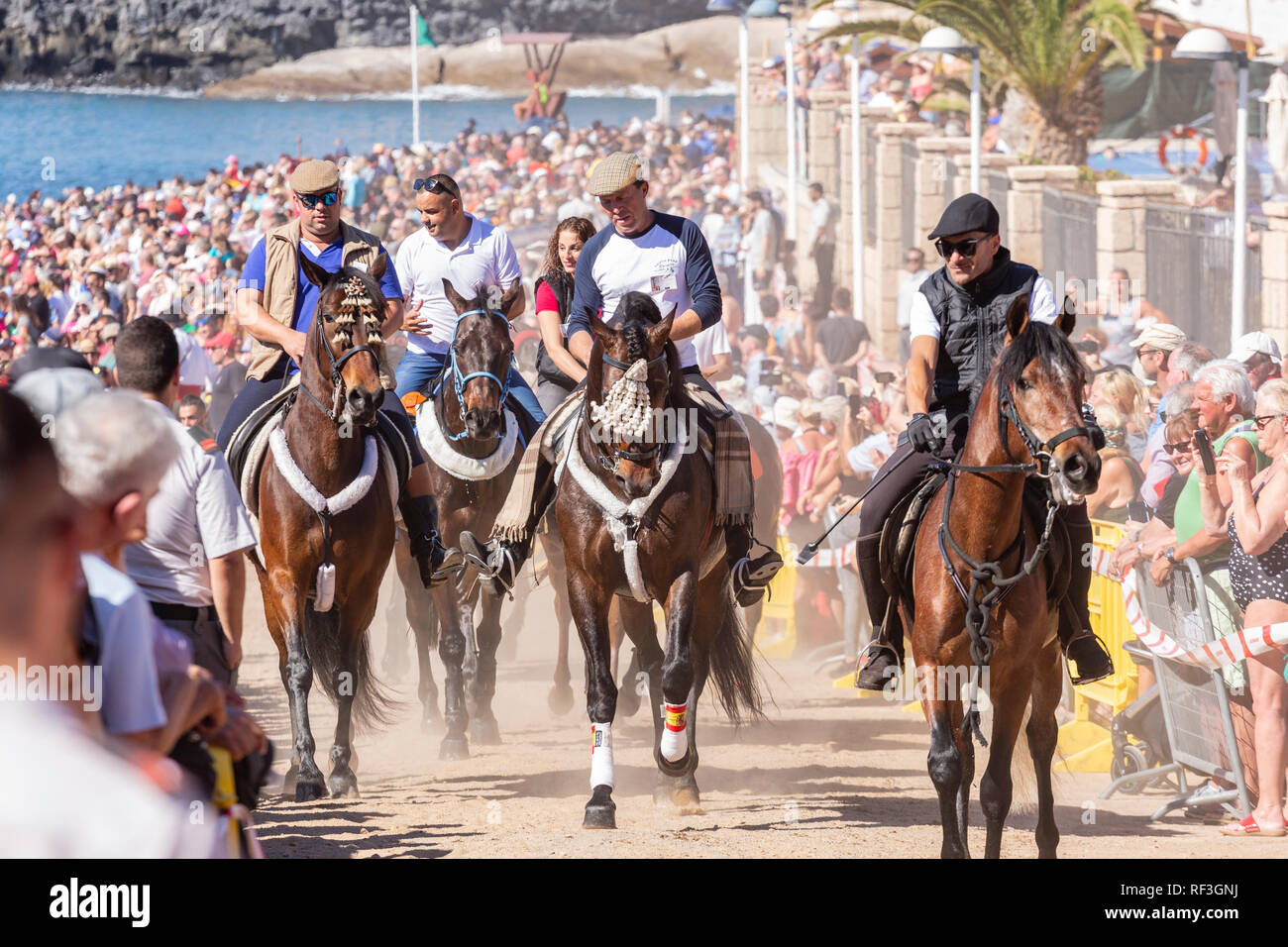 Cavalli e Cavalieri lasciando La Enramada beach dopo la balneazione i loro animali in mare a San Sebastian romeria, fieasta, La Caleta, Tenerife, può Foto Stock