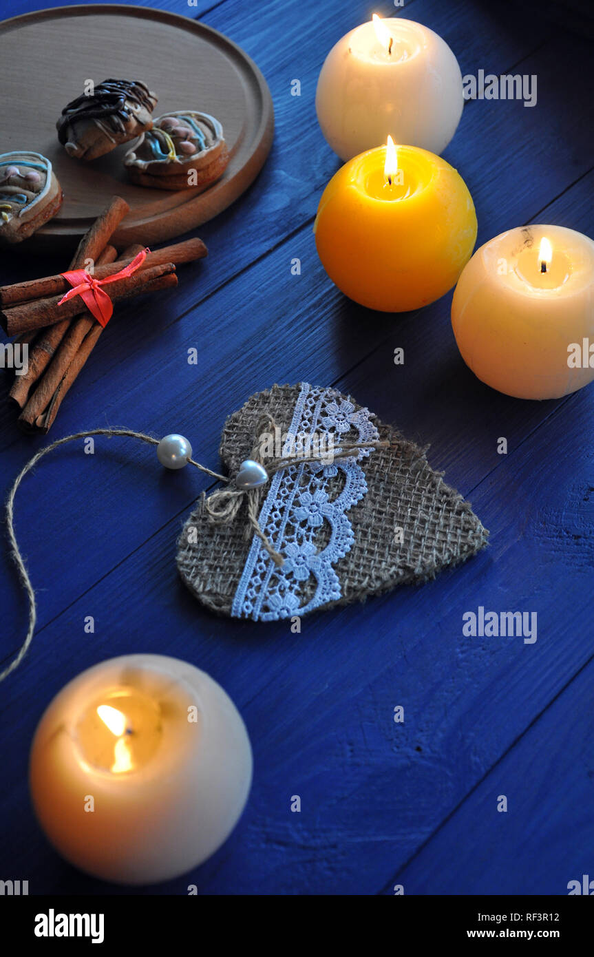 Masterizzazione di quattro candele sferiche, decorativi fatti a mano cuore, bastoncini di cannella e biscotti sul tavolo blu Foto Stock