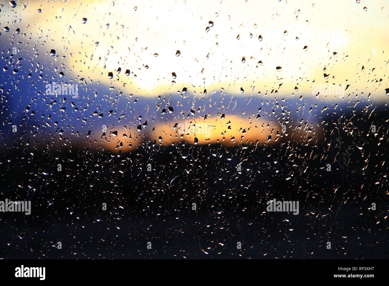 La pioggia al di fuori della finestra sul background del tramonto. Gocce di pioggia sul vetro durante la pioggia. Tramonto al di fuori finestra durante la pioggia. Texture brillanti di gocce di acqua Foto Stock