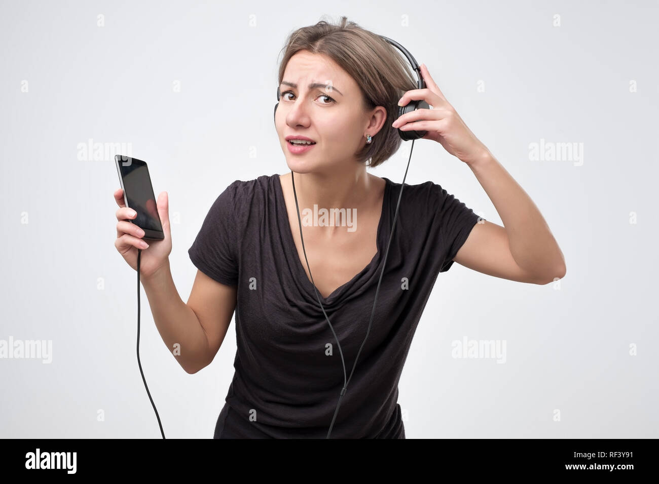 Donna ascolto di musica con le cuffie da uno smart phone e chiede cosa. Foto Stock