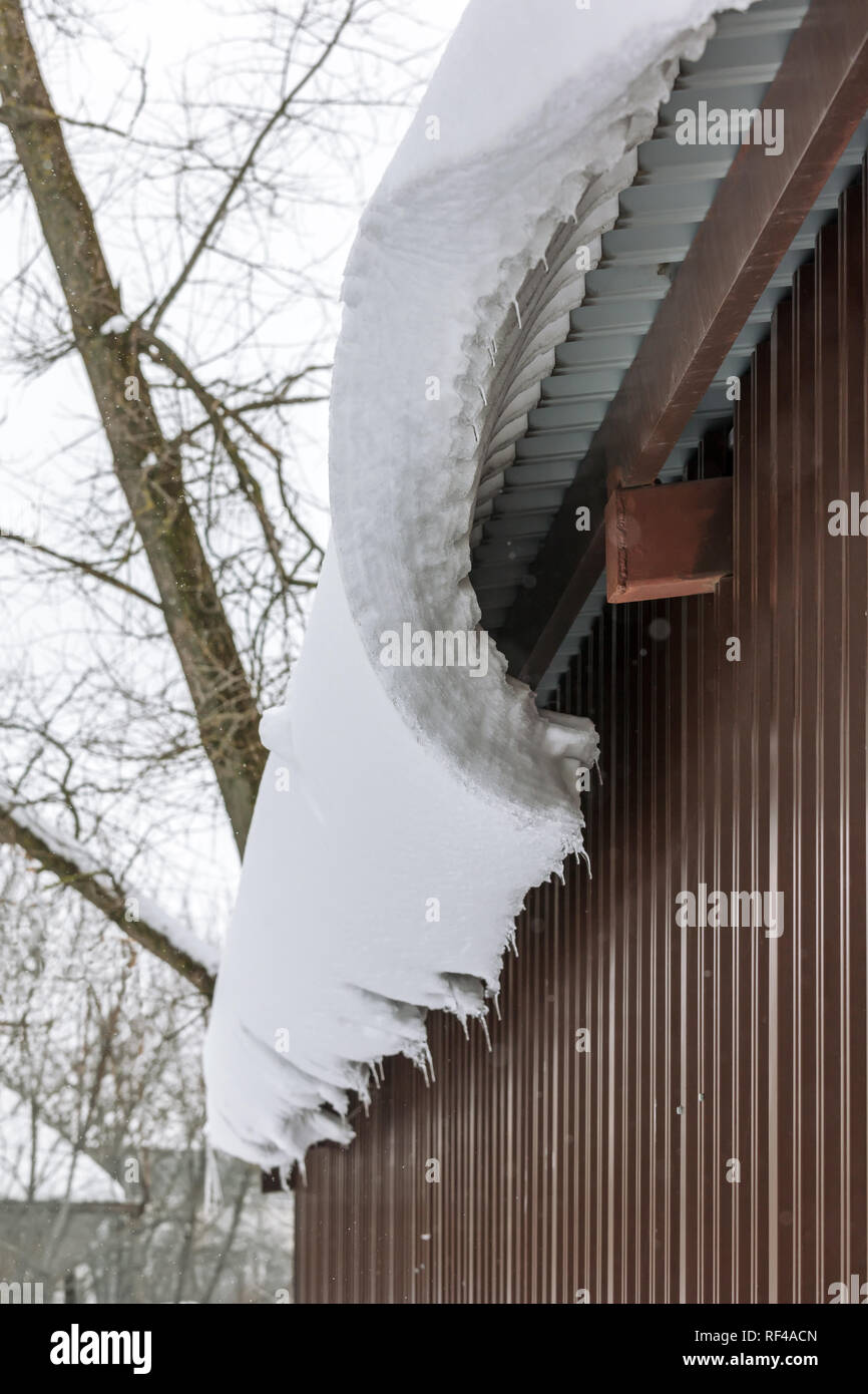 Il cumulo di neve sospesi dal tetto verso il basso. il tetto con il cornicione di neve e ghiaccioli Foto Stock