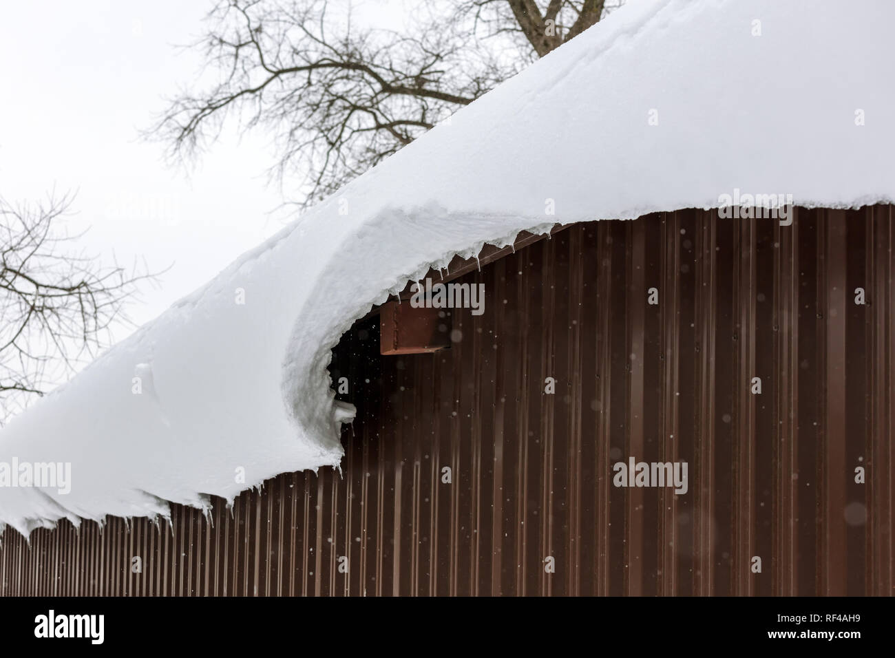 Un enorme blocco di neve pende dal tetto del capannone di metallo. cornicione di neve Foto Stock