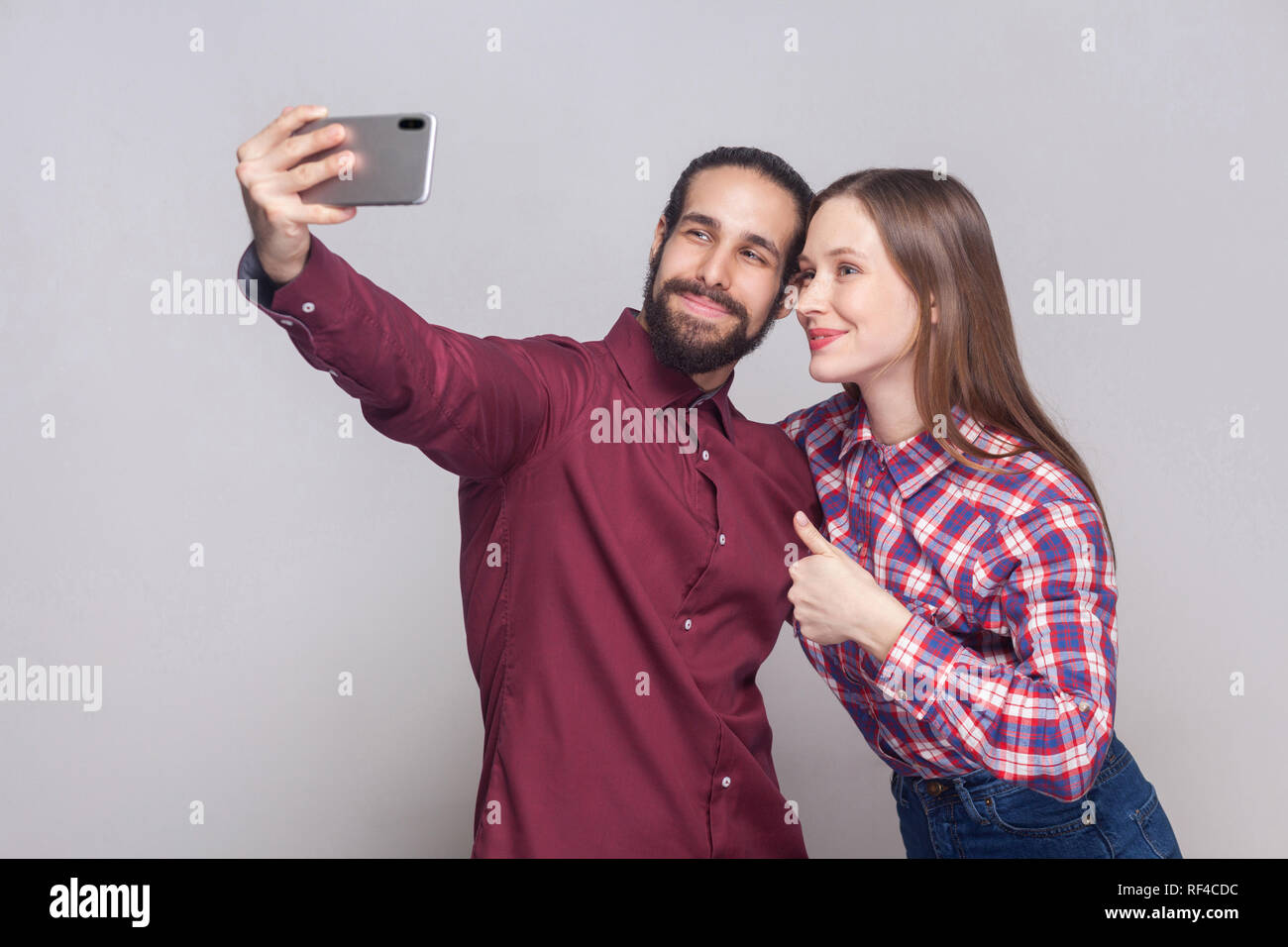 Ritratto di felice soddisfatto giovane in piedi, guardando e sorridente alla fotocamera di mobile smart phone per rendere selfie o video chiamata con il pollice in alto. interna s Foto Stock