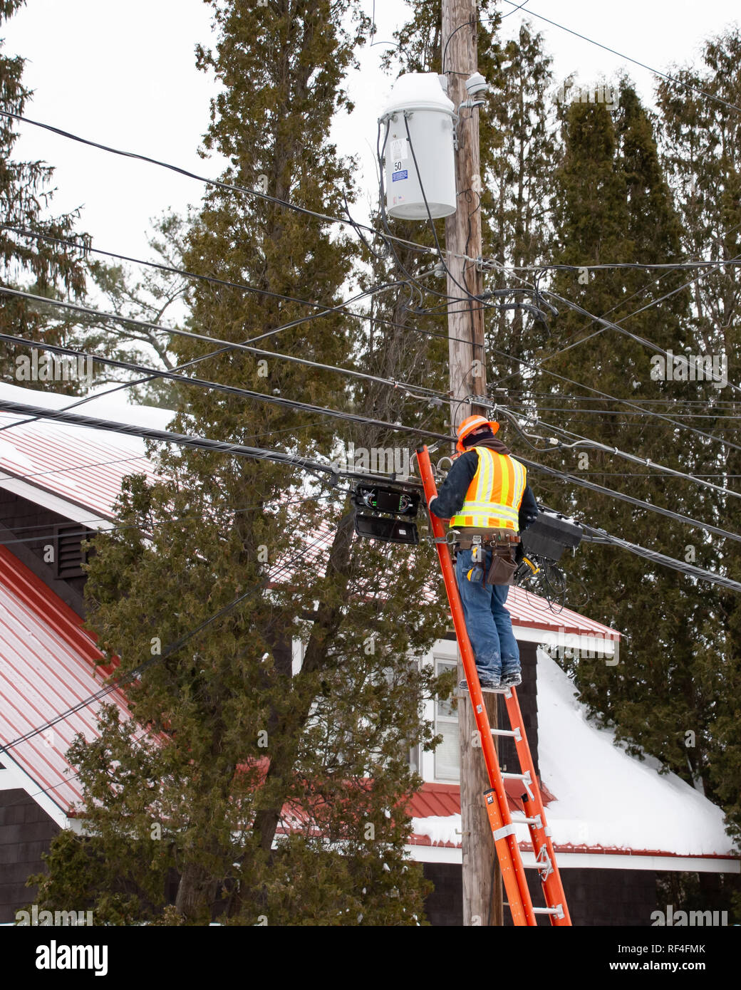 Un uomo su una scala lavorando sul cavo a fibra ottica connessioni in speculatore, NY USA in una fredda giornata invernale. Foto Stock