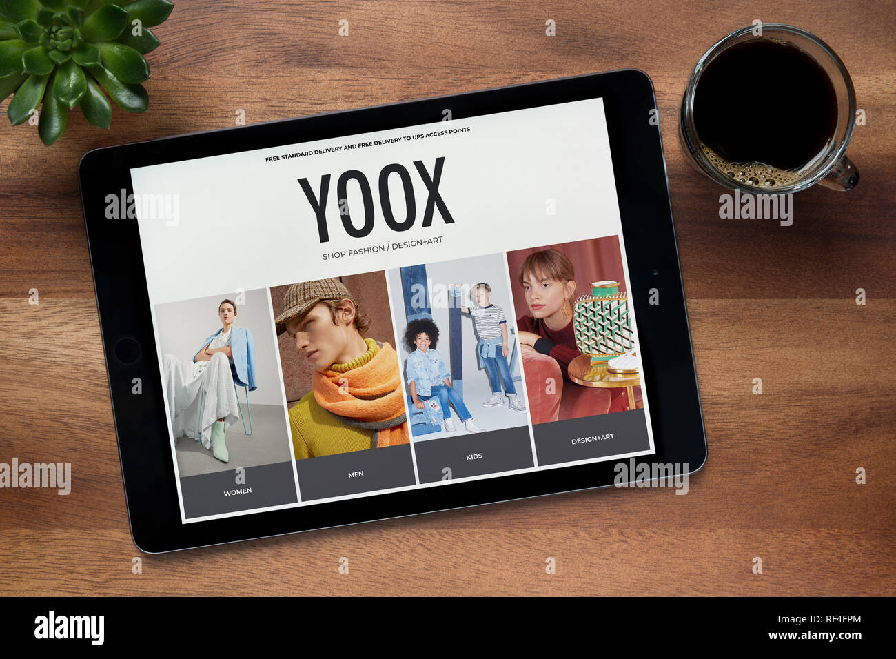 Il sito web di Yoox è visto su un tablet iPad, su di un tavolo di legno lungo con un caffè espresso e una pianta di casa (solo uso editoriale). Foto Stock