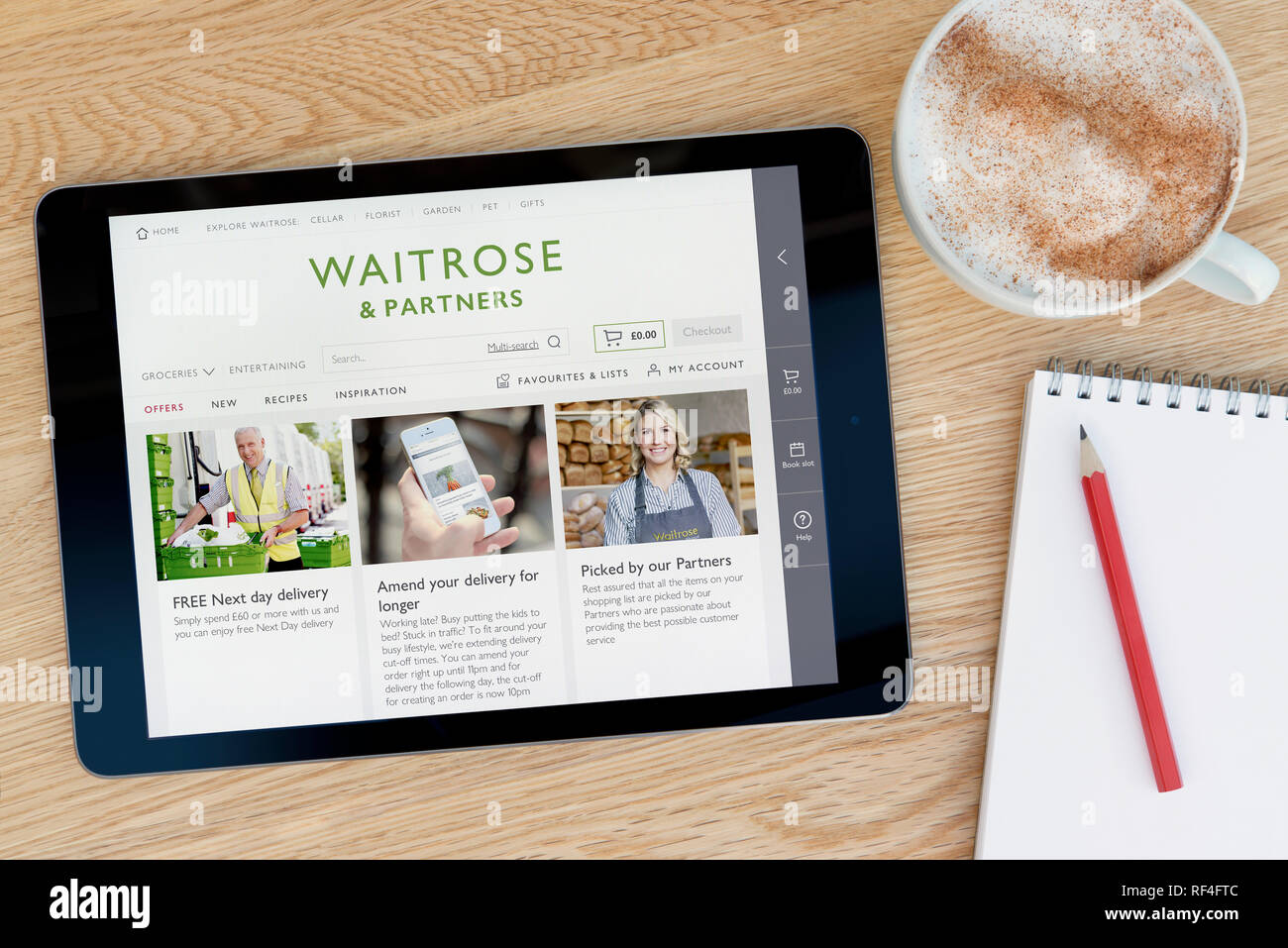 Il Waitrose e partner funzionalità del sito su un iPad dispositivo tablet pc che si appoggia su una tavola di legno accanto a un blocco note (solo editoriale). Foto Stock