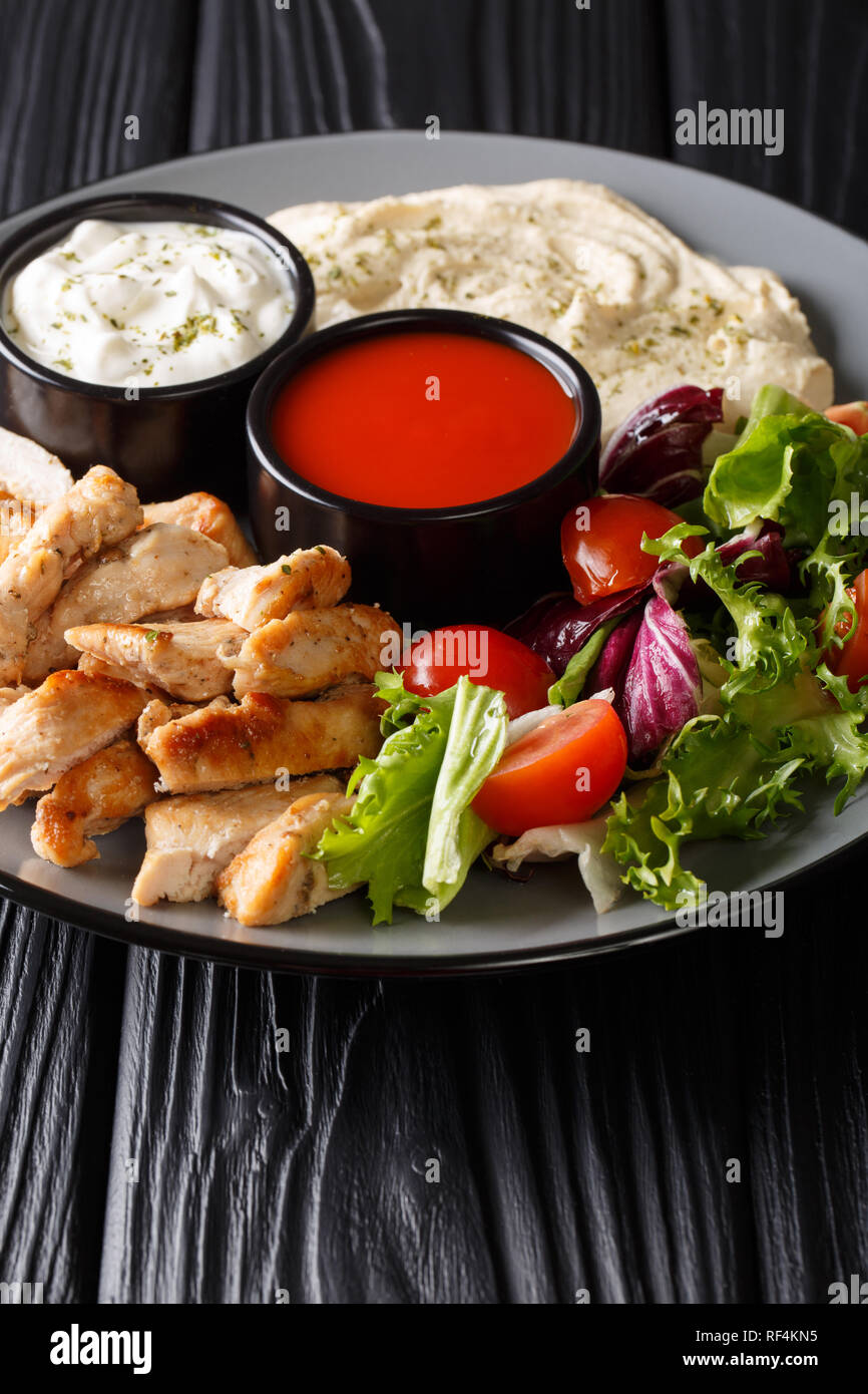 Sana piastra shawarma con pollo, hummus, insalate e salse close-up su una tavola di legno verticale. Foto Stock