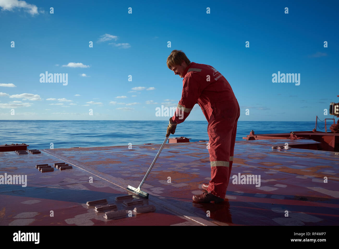 Navi i membri dell'equipaggio dipinto il coperchio esterno con un luminoso cielo blu su uno sfondo. Nave il concetto di manutenzione. Concetto di lavoro di squadra. Foto Stock