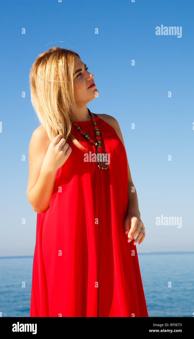 Donna bionda in abito rosso sul cielo blu sullo sfondo. Foto Stock