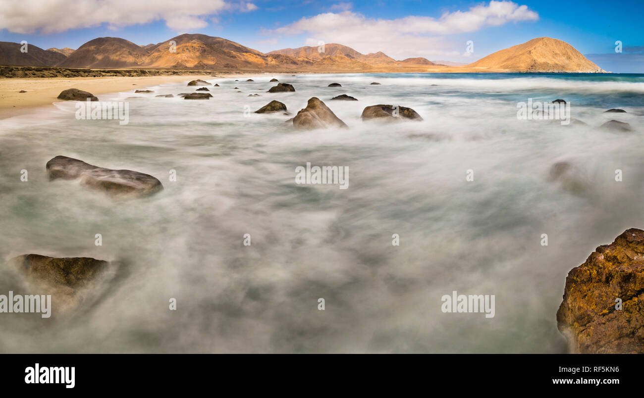 L'acqua si muove tra le rocce in una spiaggia selvaggia nel deserto di Atacama. Il movimento dell'acqua crea forme in acqua su un colpo di esposizione lungo Foto Stock