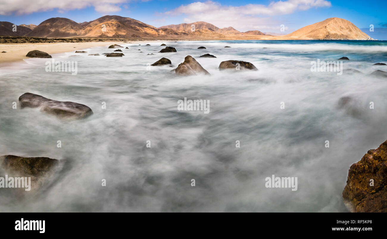 L'acqua si muove tra le rocce in una spiaggia selvaggia nel deserto di Atacama. Il movimento dell'acqua crea forme in acqua su un colpo di esposizione lungo Foto Stock