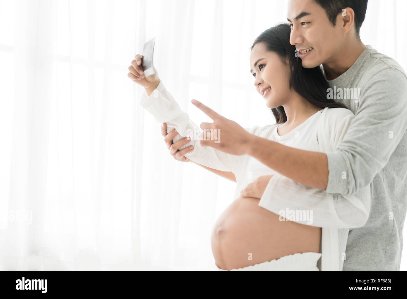 Bella asiatica donna incinta e Asian bel marito holding e cercando un sonogram in casa. Concetto di gravidanza, health care, ginecologia, medi Foto Stock