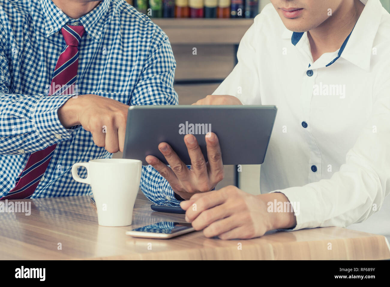 Immagine ritagliata imprenditore seduto a tavola con la tazza di caffè, tavoletta digitale e smart phone, imprenditore mani messaggio di digitazione sul touchscreen ta Foto Stock