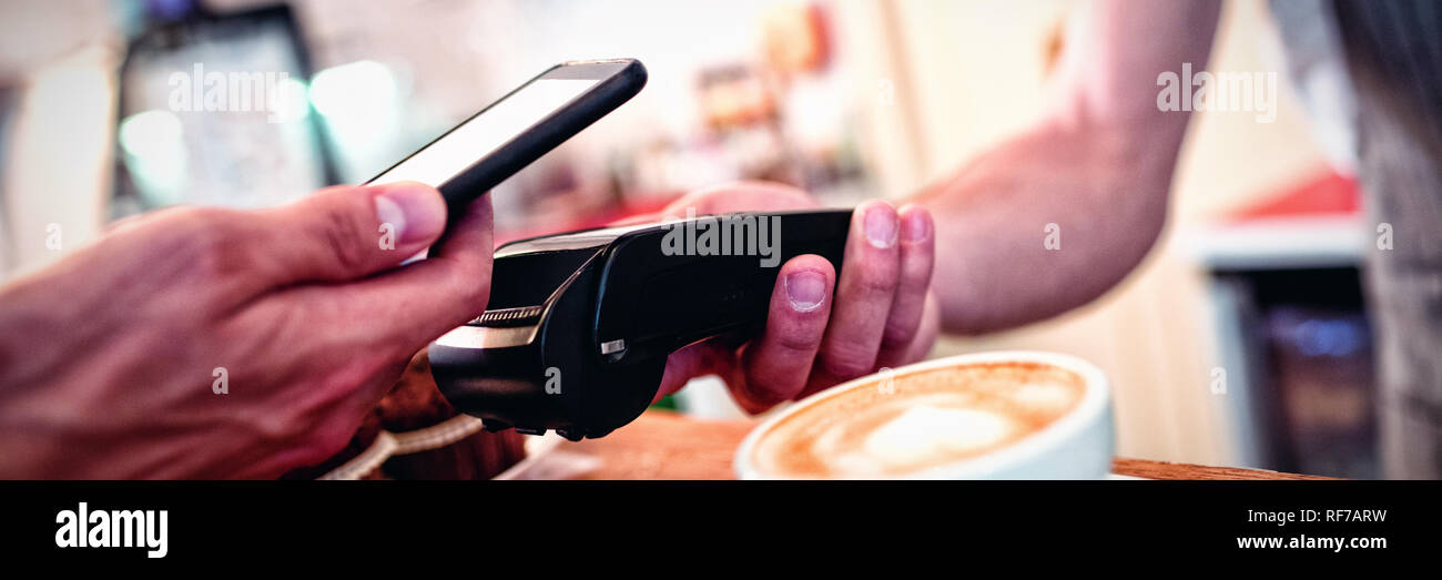Close-up del cliente con il cellulare e il barista con lettore di schede Foto Stock