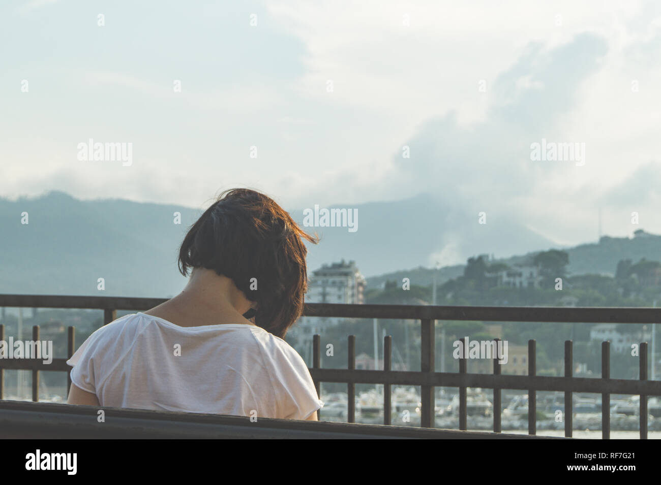 vista posteriore di una donna che inclina la testa mentre si siede su una panchina davanti al paesaggio Foto Stock