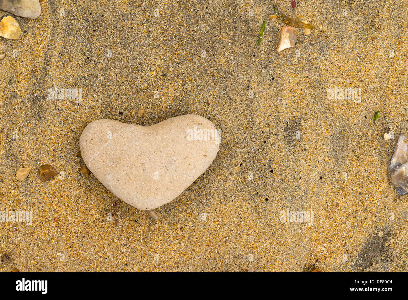 Close up di un giallo heartshaped pebble giacente su di una spiaggia di sabbia nel sud del Regno Unito Foto Stock