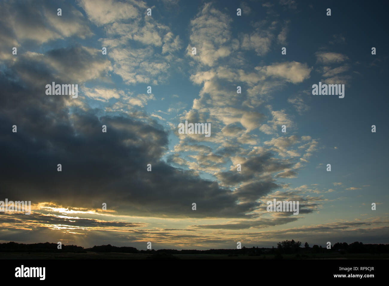 La luce del sole attraverso la rottura serata grigio nuvole nel cielo blu, skyline e albero Foto Stock