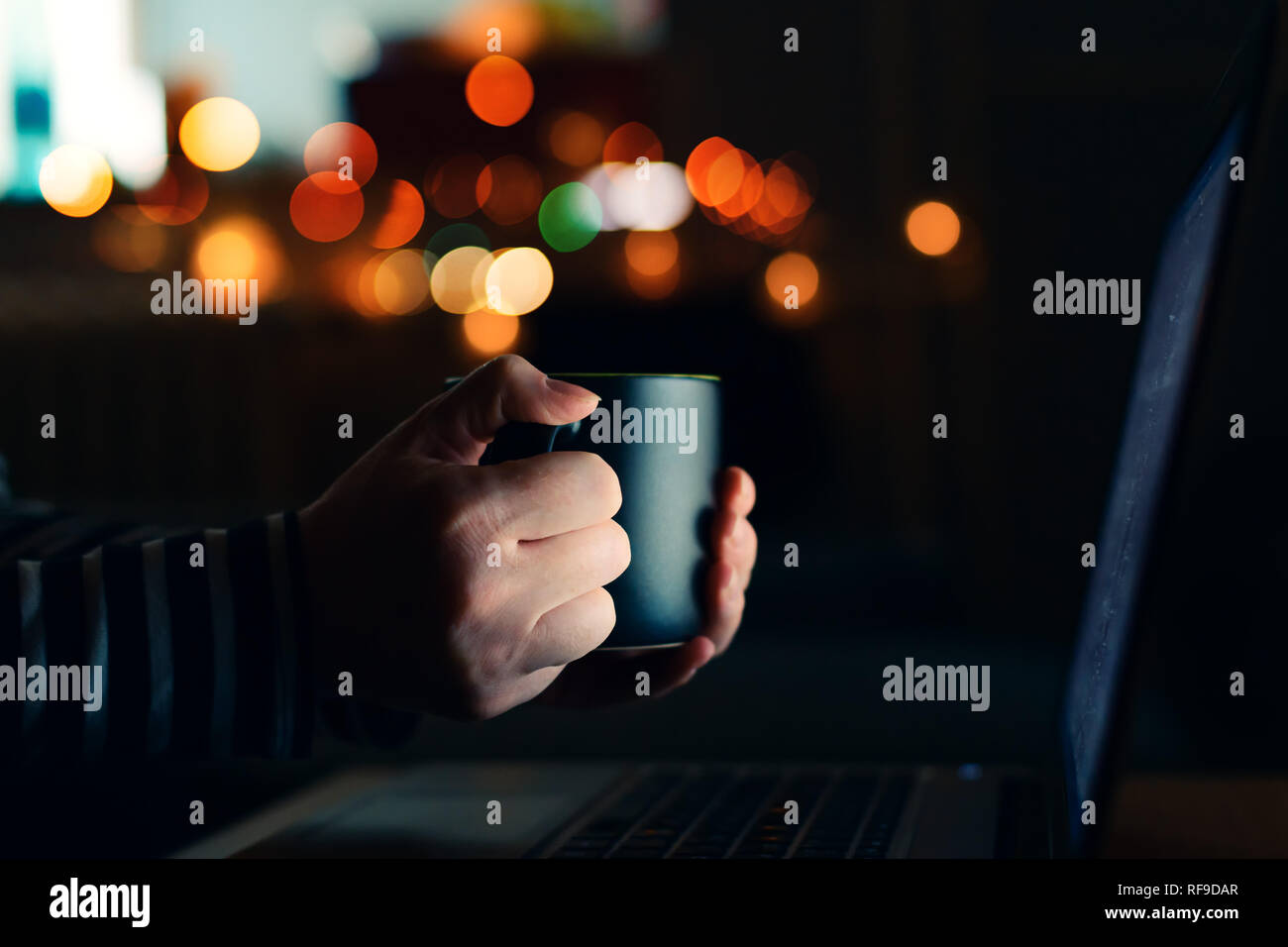 Donna con la tazza di caffè guardando il computer portatile durante la notte, in prossimità delle mani Foto Stock