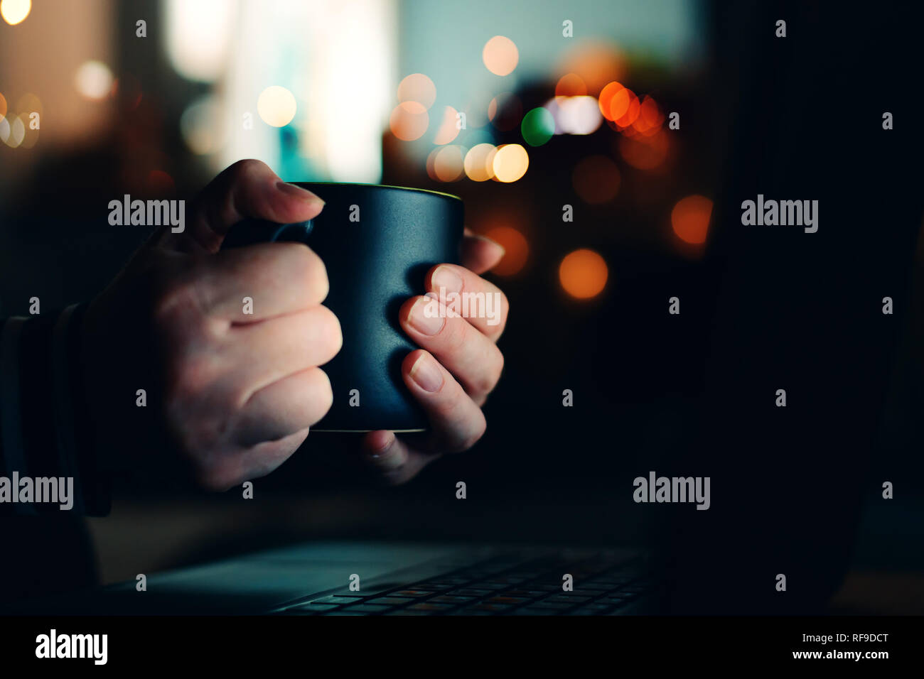 Donna con la tazza di caffè guardando il computer portatile durante la notte, in prossimità delle mani Foto Stock