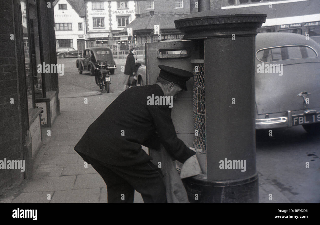 Degli anni Cinquanta, storico, GPO portalettere che indossa il tappo svuotamento di un high street post box, Inghilterra, Regno Unito. Foto Stock