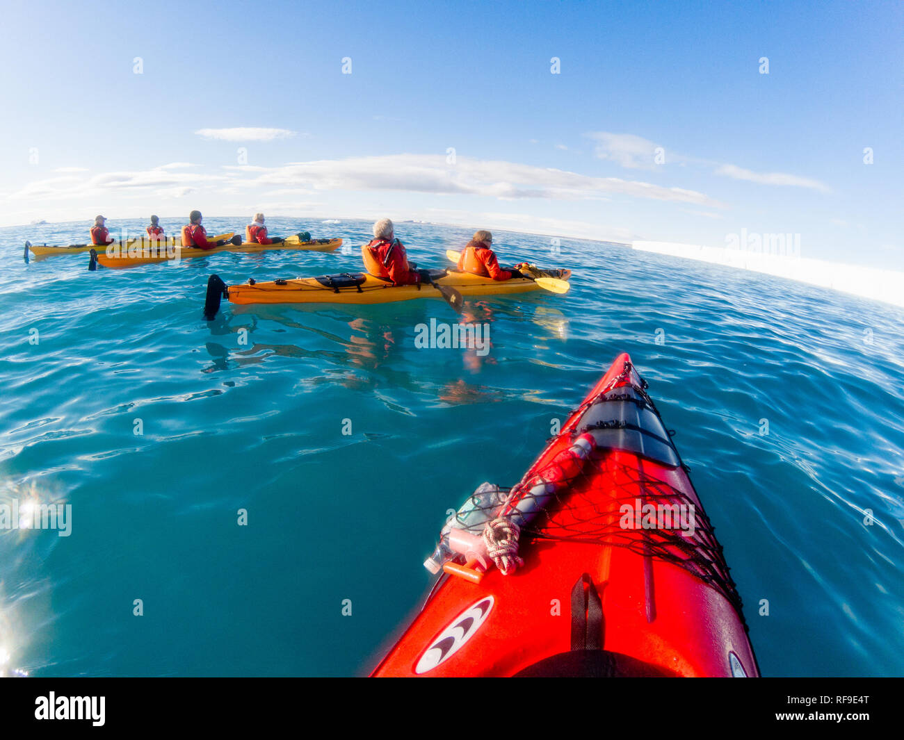 Turisti in kayak Paesaggio artico Svalbard Norvegia | SVALBARD, Norvegia — Kayakisti in mute asciutte arancioni remano in tandem su acque artiche specchianti vicino alla banchisa alla deriva al largo di Svalbard. L'arcipelago, situato più o meno a metà strada tra la terraferma norvegese e il Polo Nord, è diventato un centro per le spedizioni in kayak di piccoli gruppi che portano i pagatori vicino alle fronti glaciali e alla banchisa senza il rumore o il risucchio di un motore. Foto Stock