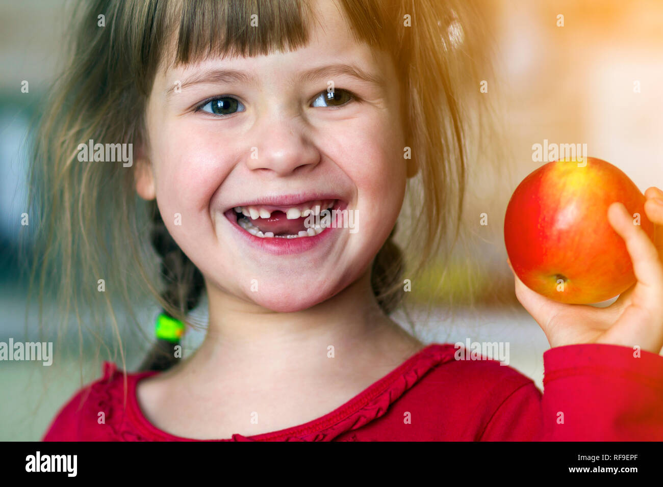 Un Grazioso Piccolo Ricci Ragazza Sdentati Sorrisi E Mantiene Una Mela Rossa Ritratto Di Un Bambino
