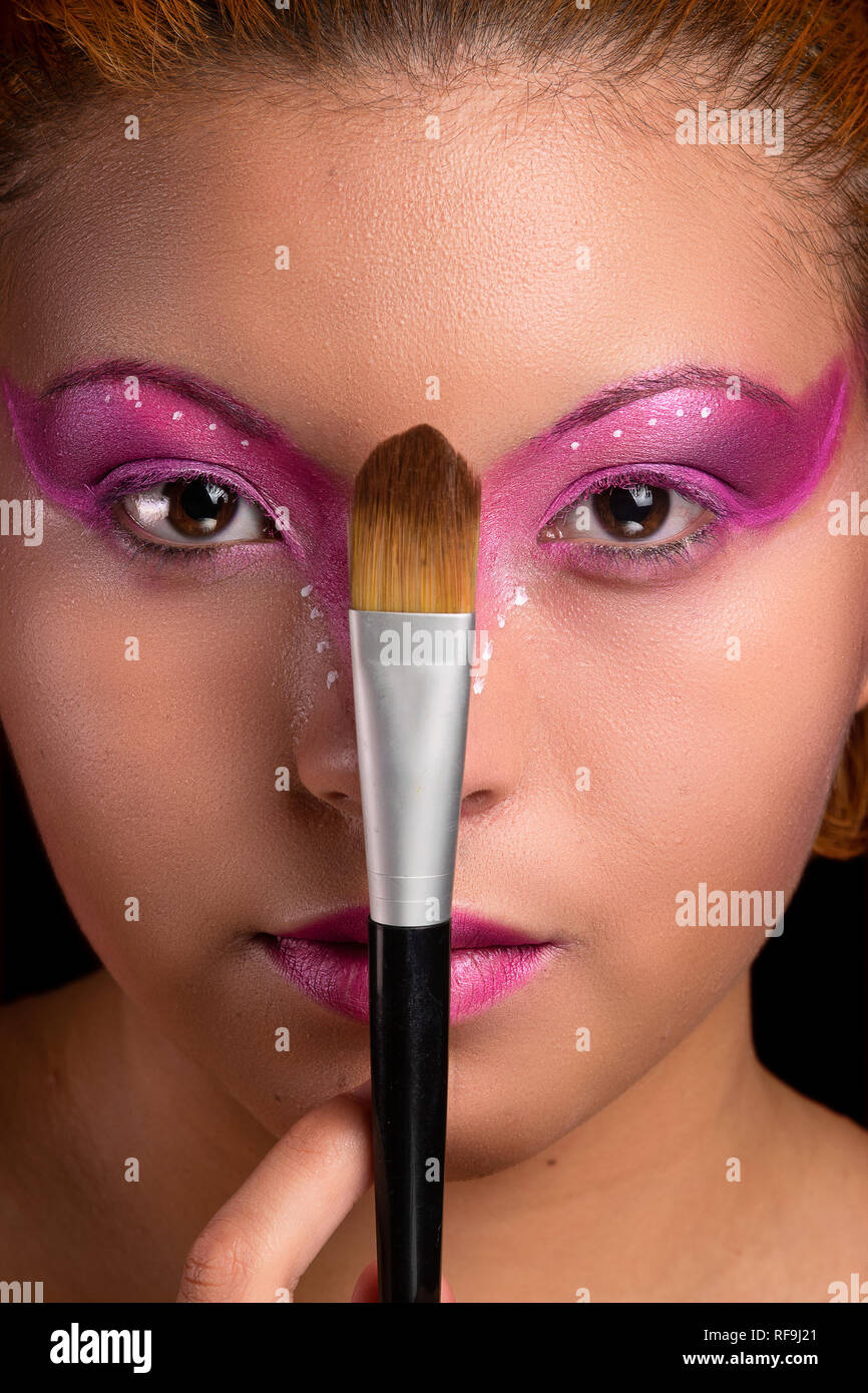 Giovane e bella ragazza ritratto, con viola e rosa trucco, closeup, tenendo una spazzola vicino alla faccia, guardando la telecamera Foto Stock