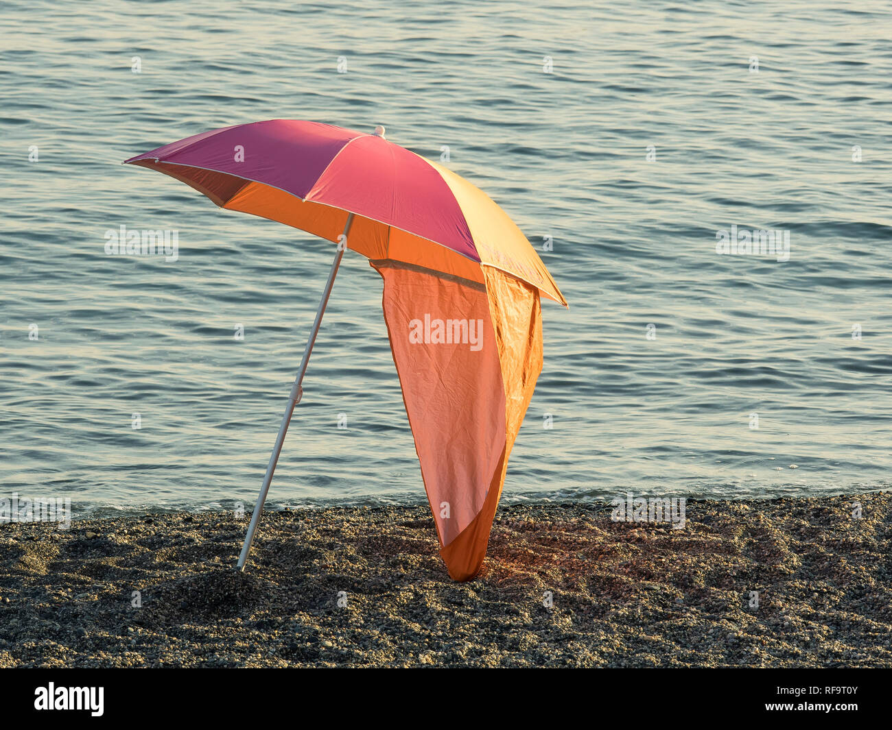 Colorato parasol (ombrellone) isolato su una spiaggia di ciottoli al  tramonto la calma acqua di mare in background Foto stock - Alamy