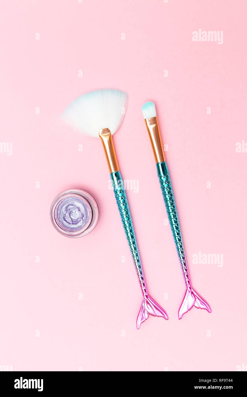 Spazzola per il trucco mermaid e violetta ombretto su sfondo rosa. In verticale Foto Stock