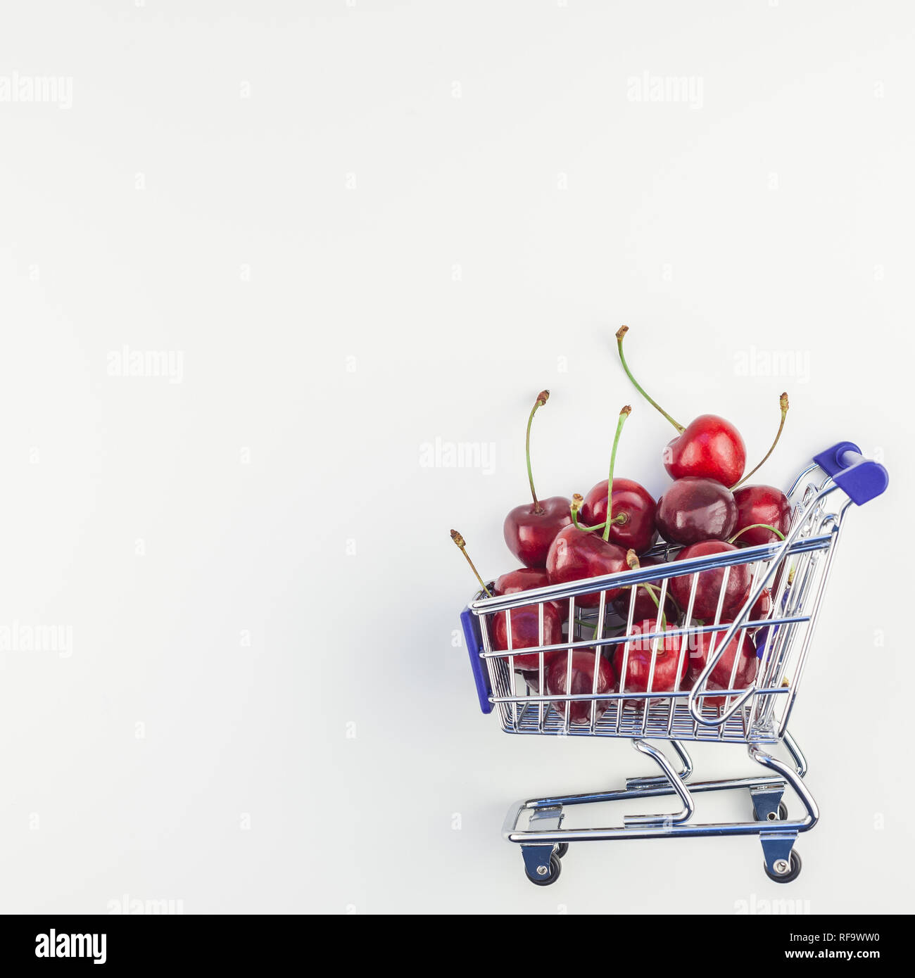 Immagine quadrata di ciliegie mature in un carrello della spesa con copia spazio isolato su sfondo bianco in stile minimal. Concetto di supermercato o mercato di frutta Foto Stock