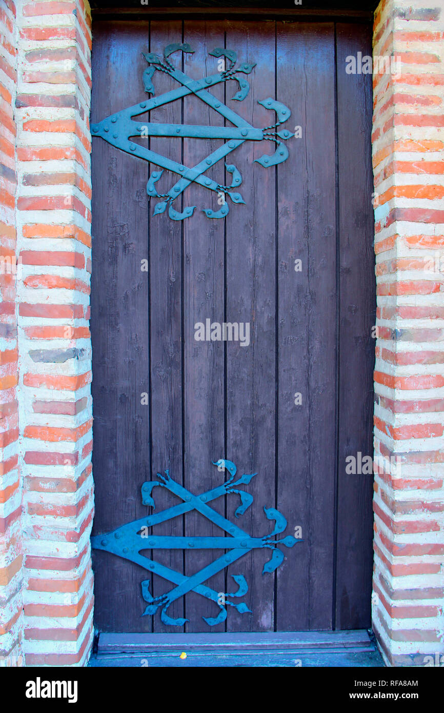 Antica porta di legno con ferro forgiato la cerniera. Vecchia chiesa porta che conduce al luogo religioso realizzato dal rosso mattone. Muro di mattoni rossi con la vecchia porta di legno Foto Stock