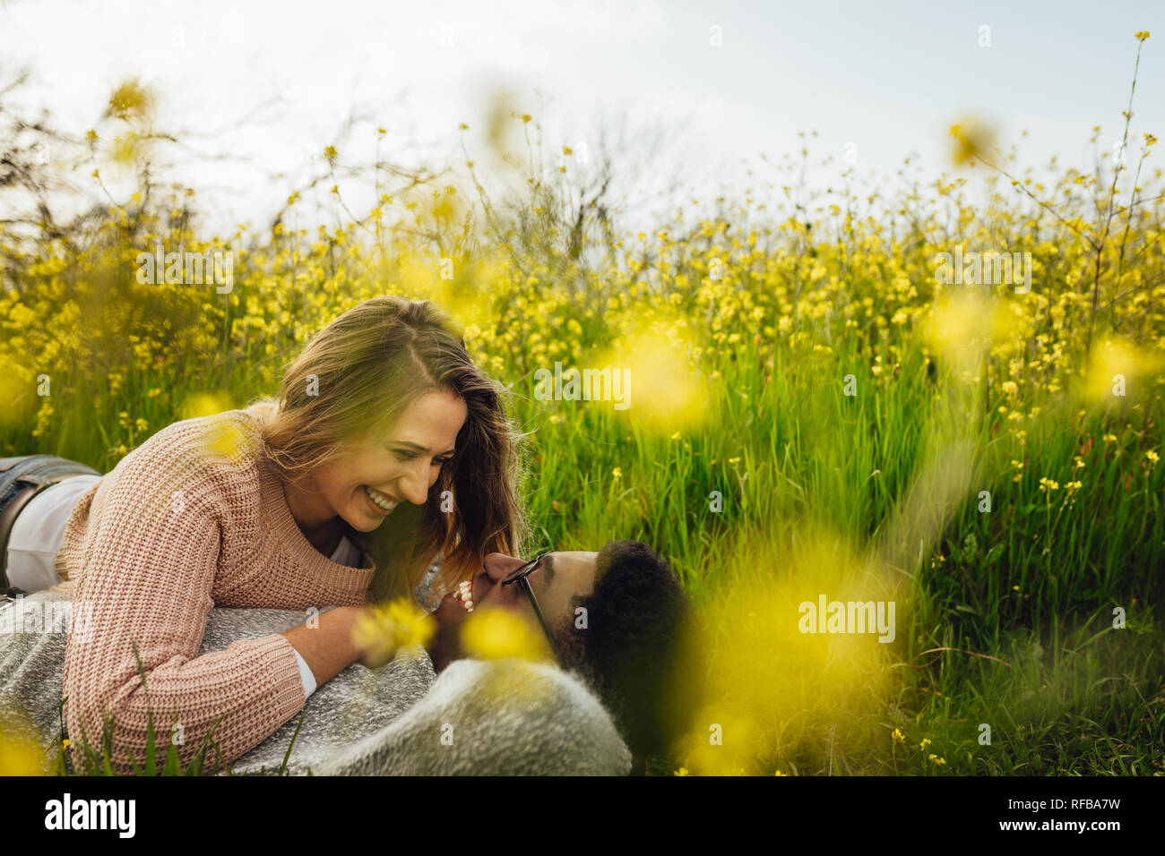 Giovane donna giaceva con il suo fidanzato sull'erba alta e sorridente. Amare giovane sdraiati sull'erba guardando ogni altro e sorridente. Foto Stock