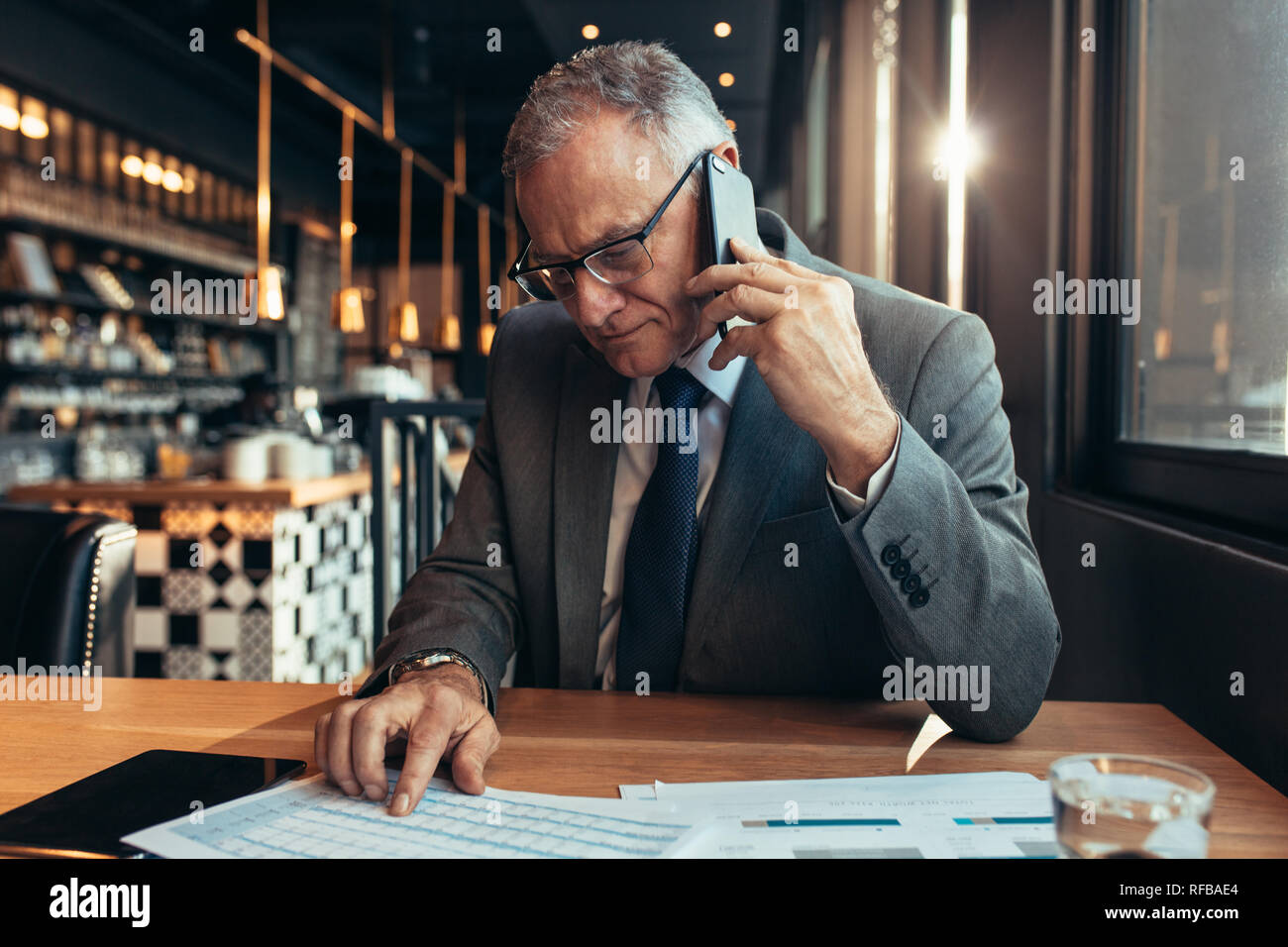 Gli imprenditori Senior seduto presso il cafe parlando al cellulare per discutere di affari nelle figure. Coppia imprenditori presso la caffetteria la lettura del documento e rendendo Foto Stock