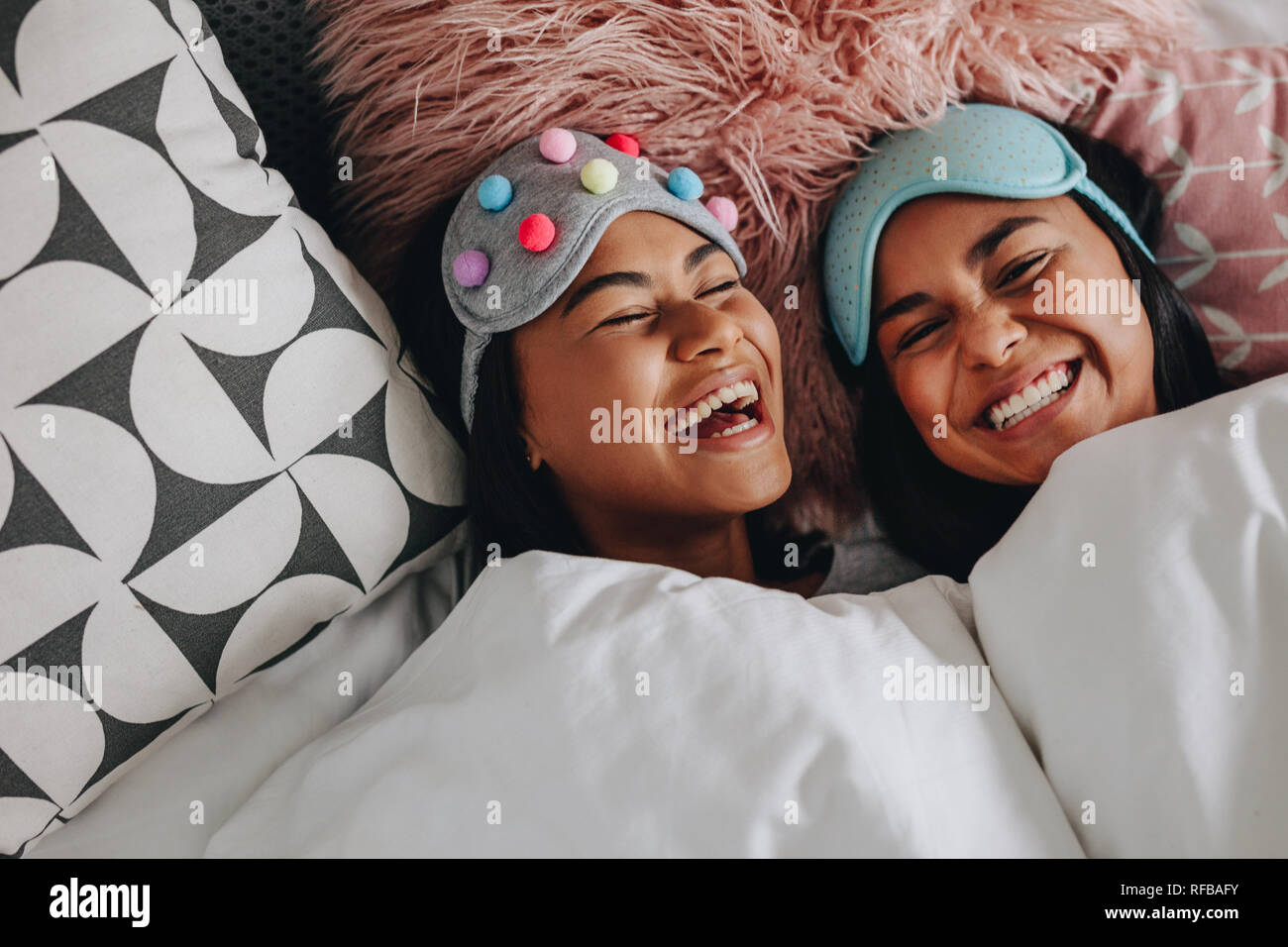 Vista dall'alto di due ragazze di ridere con gli occhi chiusi giacente sul letto avente una sleepover. Ragazze con fantasia le maschere di sospensione sopra la testa a ridere e divertirsi du Foto Stock