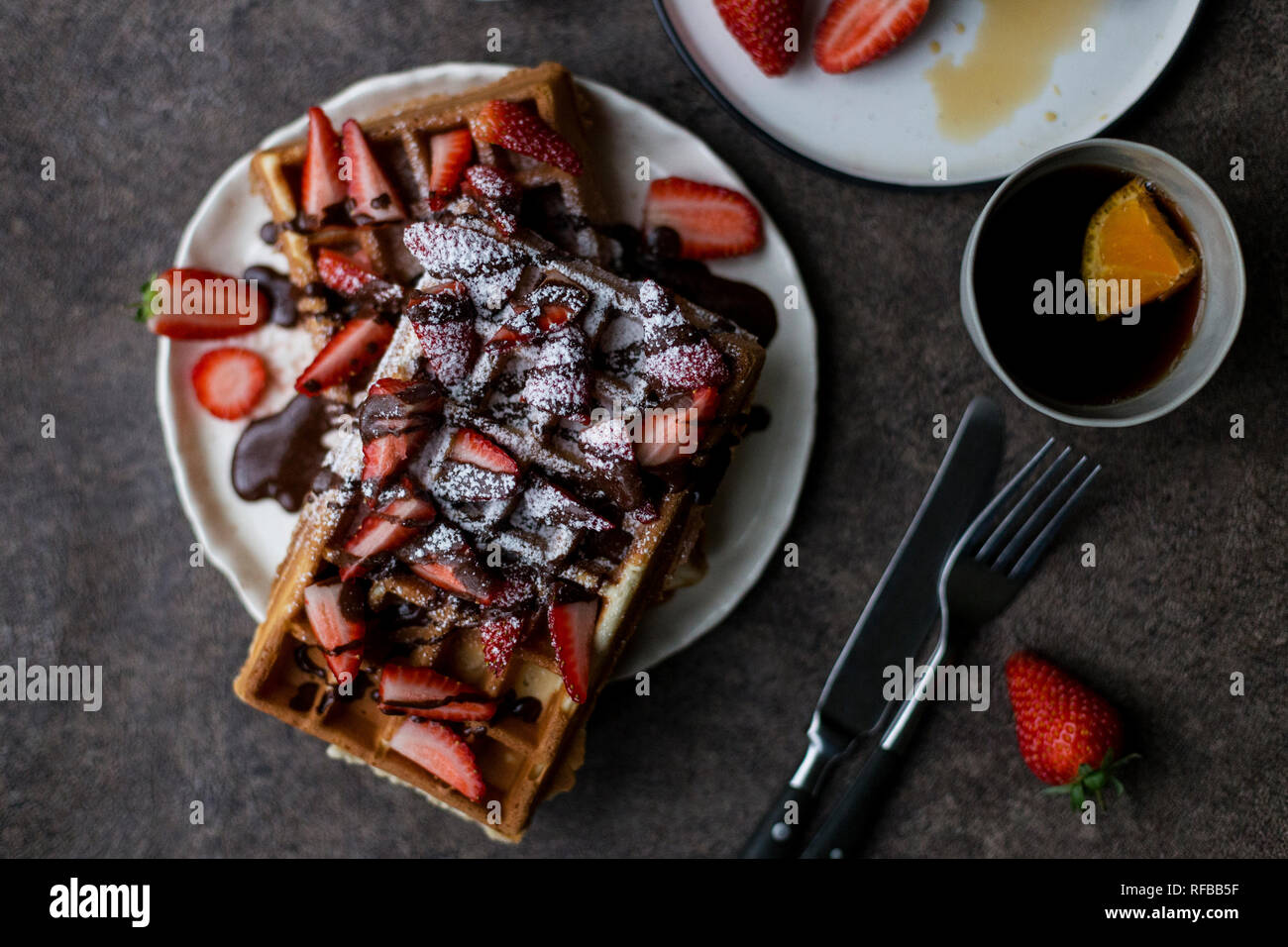 Colazione romantica con cialde belghe con fragole e cioccolato, con due tazze di tè con limone, forchetta e coltello vicino a sfondo scuro. Concep Foto Stock
