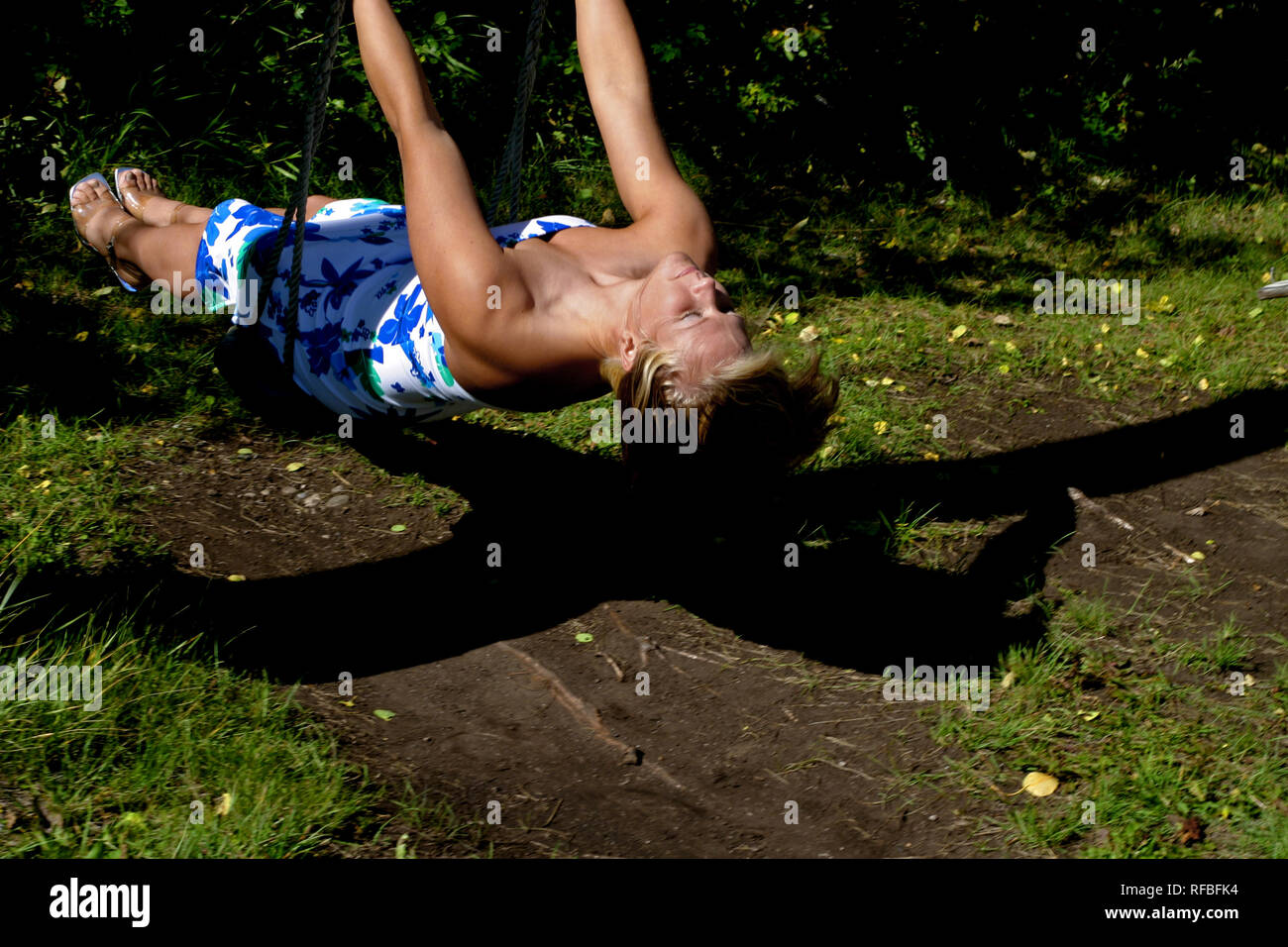 Bella donna bionda su una oscillazione in una zona alberata Foto Stock
