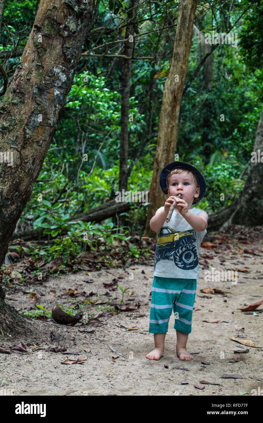 Un ragazzino con una buona immaginazione soffia un ramo di albero come era un vero e proprio strumento musicale. Nella splendida foresta di Manzanillo National Park Foto Stock