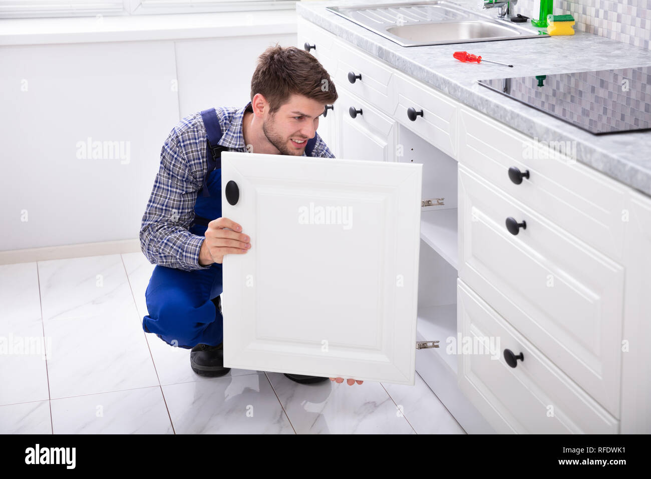 Sorridente tuttofare il montaggio di una nuova porta al di sotto del piano di lavoro della cucina Foto Stock