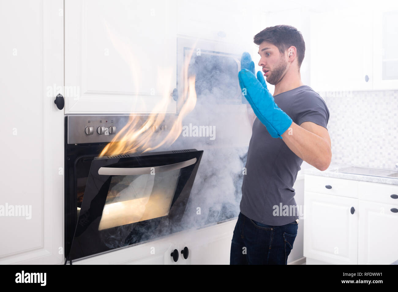 Paura giovane uomo Guardando il fuoco che esce dal forno in cucina Foto Stock