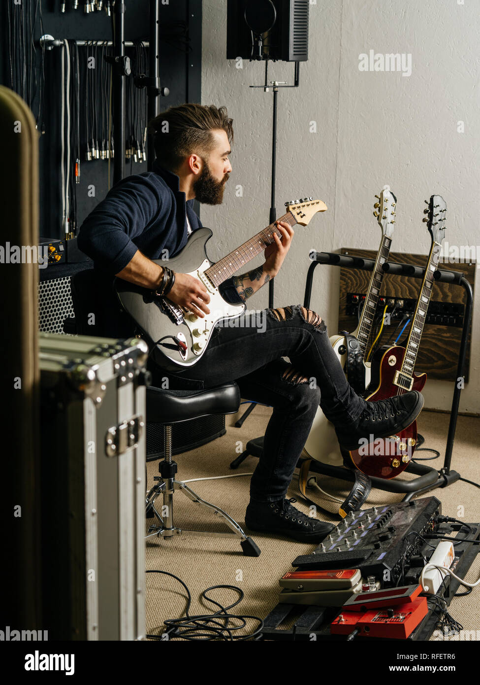 Foto di un uomo con la barba seduto e a suonare la chitarra elettrica in uno studio di registrazione. Foto Stock